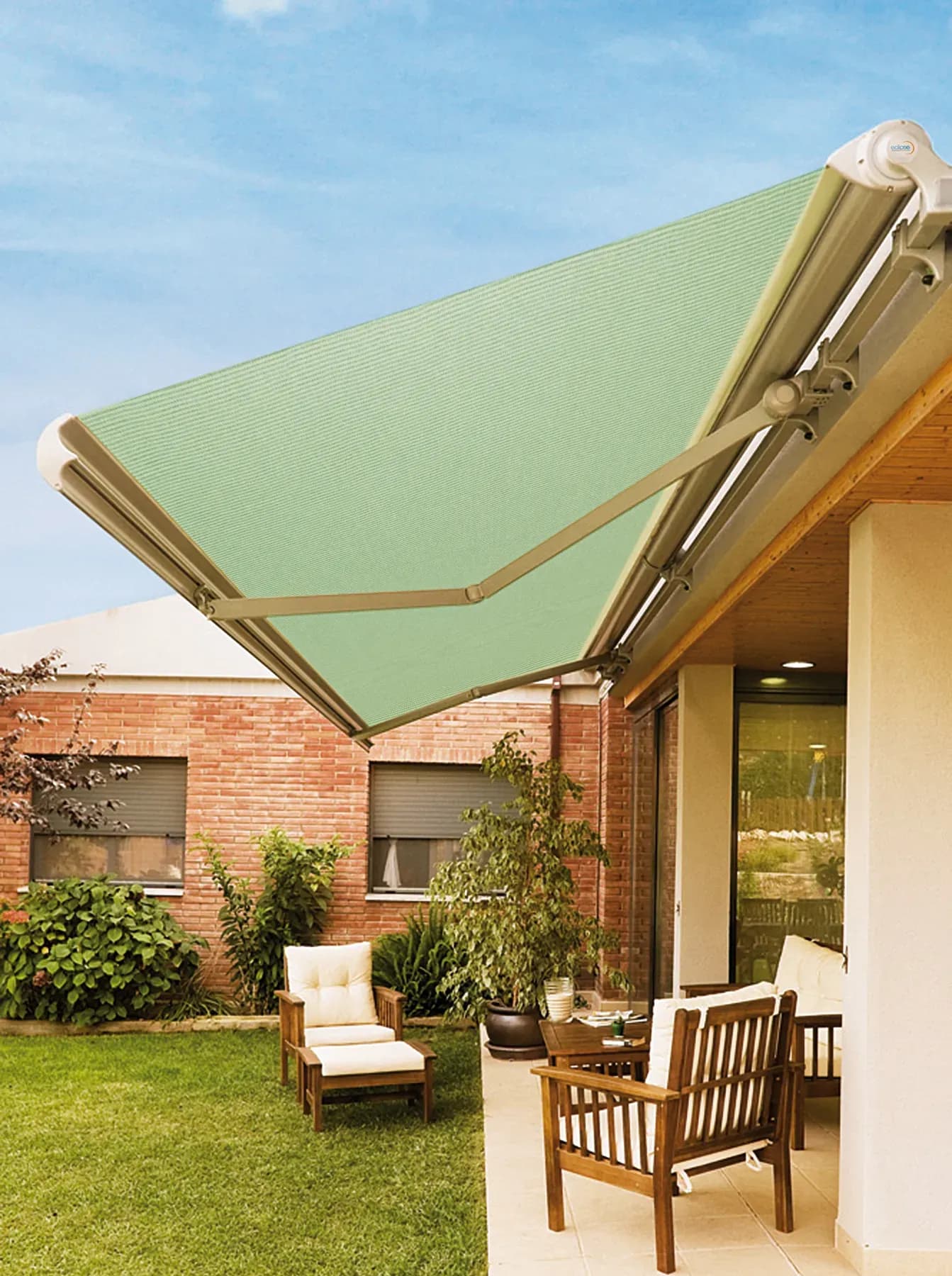 A light green retractable awning over a patio and backyard off a red brick house.