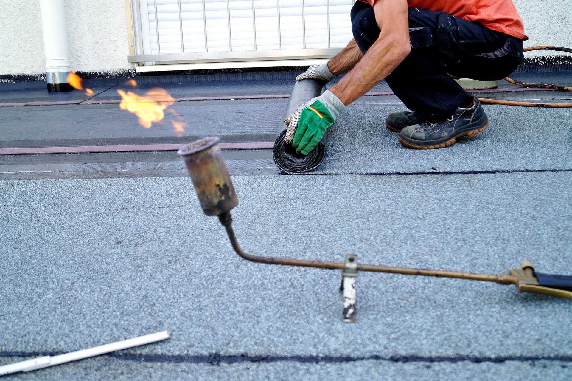 A worker unrolls and installs new commercial roofing.