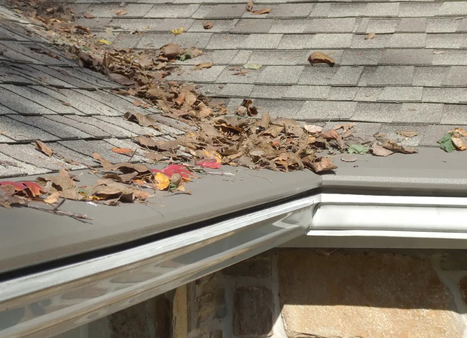 A close-up of white gutters with new light gray gutter covers on a tan stone house.