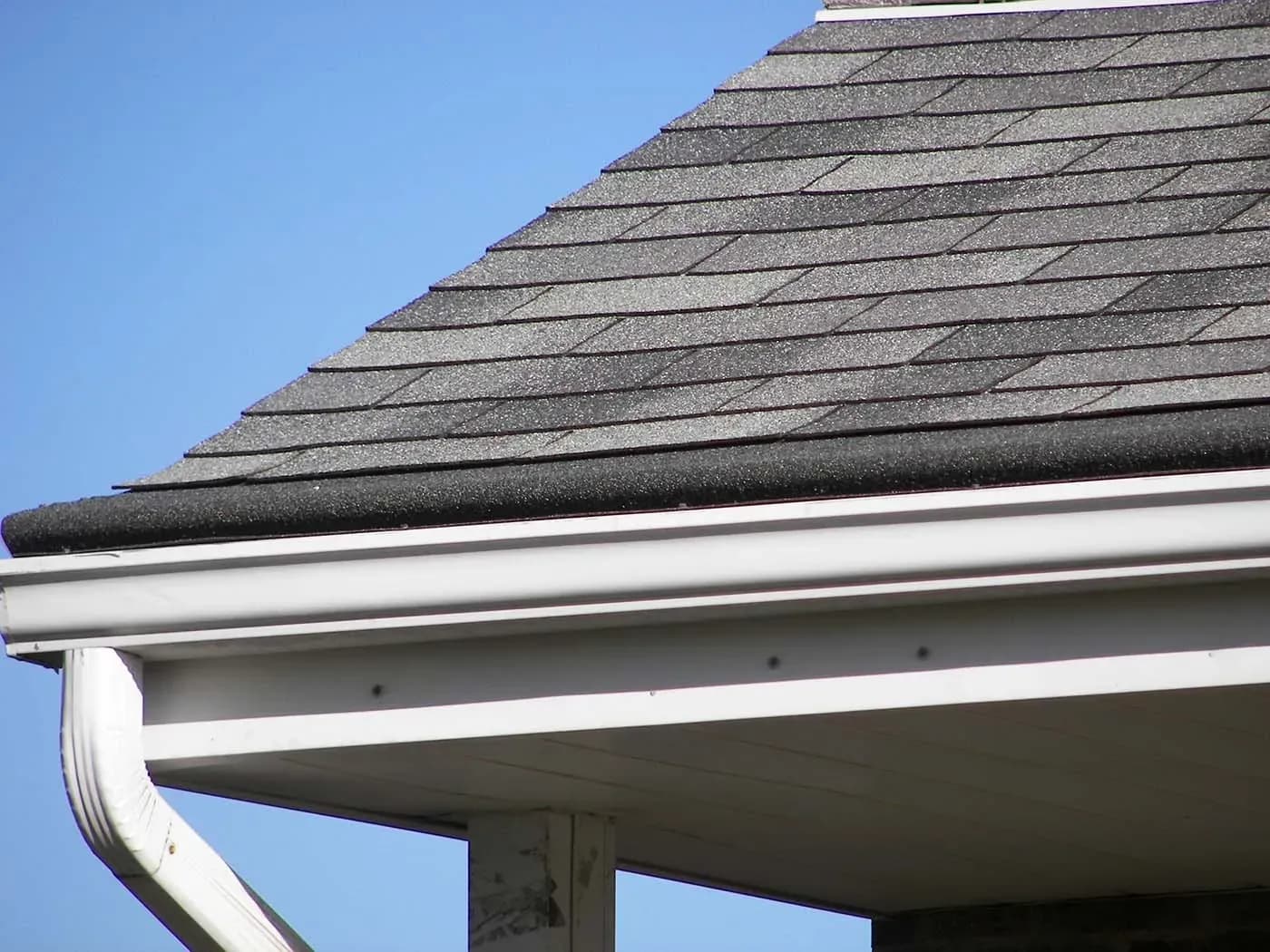 A close-up of the corner of a house with new light gray shingle roofing.