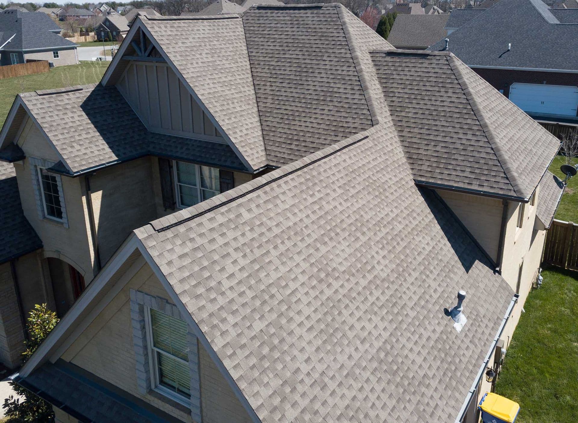 An overhead view of a new light gray shingle roof on a tan brick house.